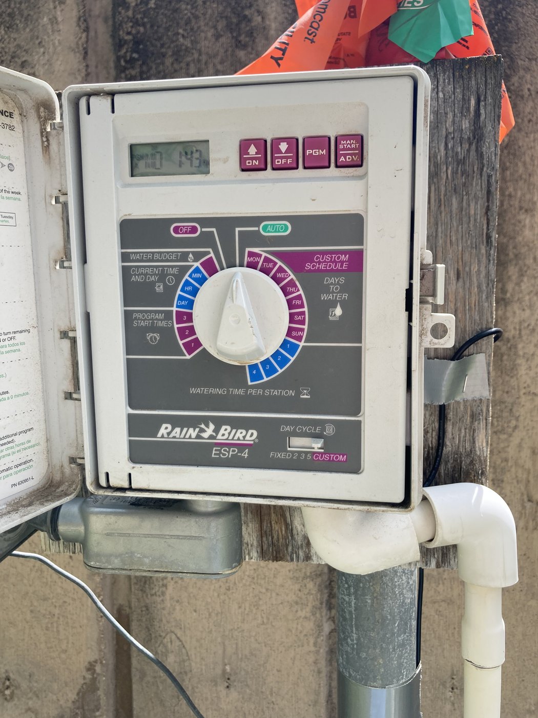 Same Rain Bird ESP-4 controller with the outer lid open, exposing the programming face — rotary dial, PGM and Manual Start buttons, LCD readout for run times.