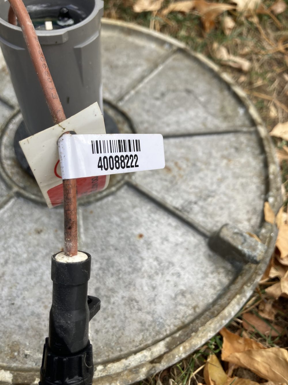 Close-up of an ORION endpoint's copper data wire crossing a galvanized meter lid, with a white barcode label clipped around the wire showing the meter serial number 40088222.